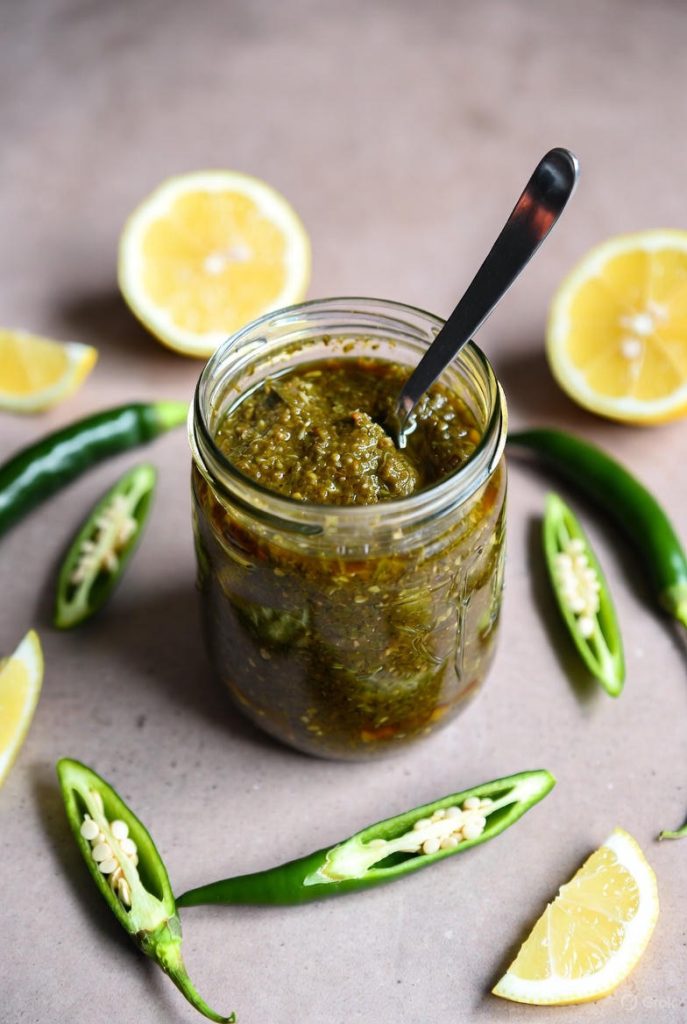 Thick green chutney in glass jar with lemon and chilies
